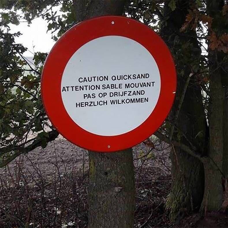 Ein Schild, das in drei Sprachen vor Treibsand warnz und als deutschen Text "herzlich wilkommen" stehen hat. 